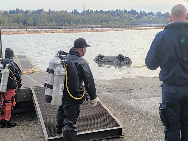 A partially submerged vehicle is being towed out of the Fraser River as two divers look on
