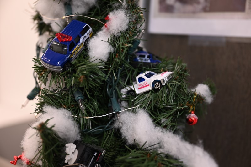 A closeup photo of a Christmas tree with fake snow and several small police vehicle ornaments including an SUV and pickup truck