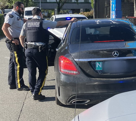 two Richmond RCMP officers conduct a road check beside a black Mercedes sedan with a green <q>N</q> sign on the back
