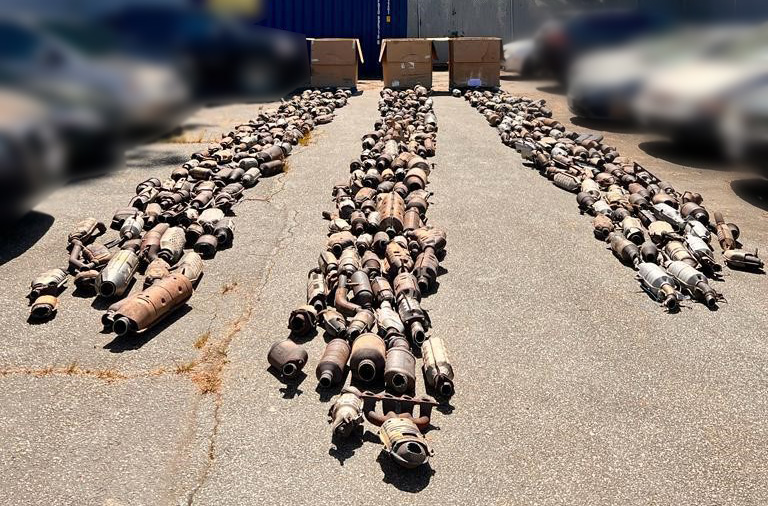 A large number of catalytic converters laid on the pavement outdoors.