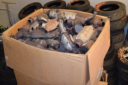 A large number of catalytic converters in a box indoors near a pile of tires.