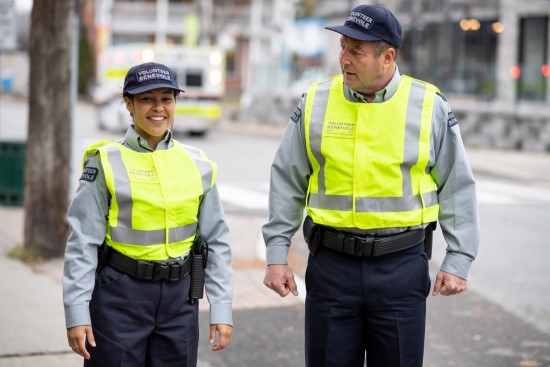 man and woman auxiliary volunteers standing together on the sidewalk wearing uniforms with reflective vests.