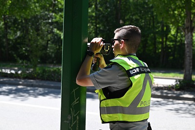A police officer in a reflective yellow vest uses a speed radar beside a road