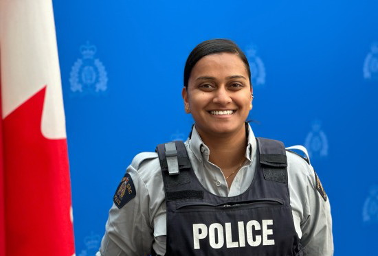 La gendarme Pancharatnarajah portant son uniforme de la GRC en souriant, avec un drapeau canadien à l’avant-plan