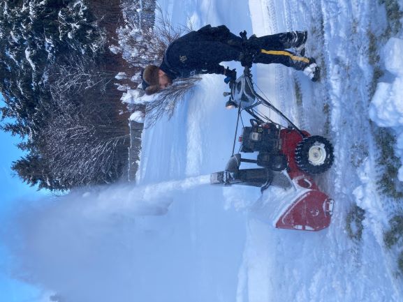 Cst Gunn from the Queen Charlotte RCMP using a snow blower to clear driveways.