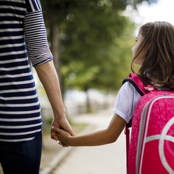 female child wearing a backpack holding her mom's hand walking to school