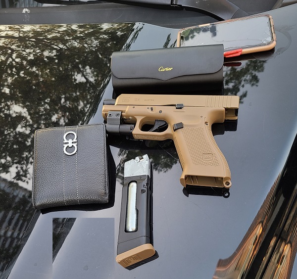 <q>Photo of firearm, magazine, wallet, sunglass case and cell phone on hood of car</q>