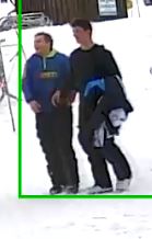 two suspects walking together; one in a blue jacket and the other carrying his jacket and dressed in black.
