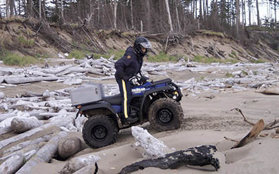 Un membre en VTT sur une plage couverte de bois flotté.