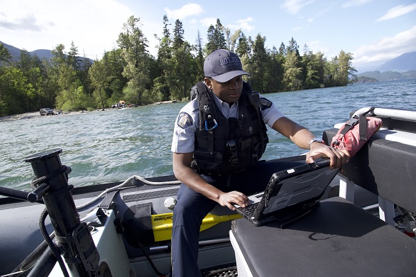 Le gendarme Berthier Kyobela travaille à un ordinateur portable pendant qu’il est assis dans l’embarcation Zodiac de la GRC en Colombie Britannique, sur le lac Harrison, au site de camping Limbert Rocks.