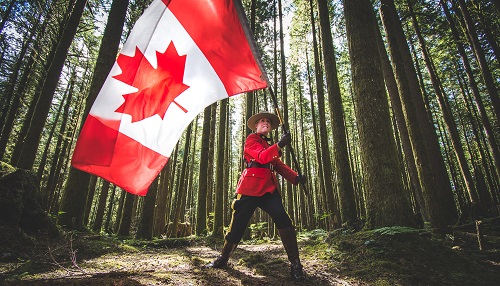 photo of RCMP officer in red serge waving Canadian flag in the woods