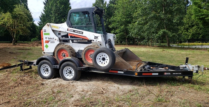 White and orange Bobcat510 skid-steer loaded onto four-wheeled trailer