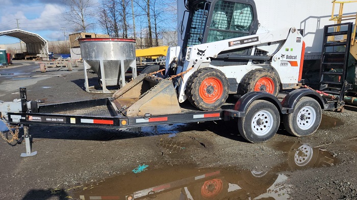 Chargeur à direction à glissement blanc, noir et orange Bobcat S510 sur une remorque garée dans un parc de stationnement en gravier