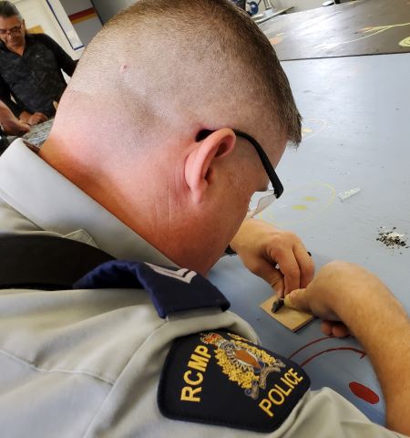 An over-the-shoulder image of a uniformed officer chipping away at a piece of obsidian. 