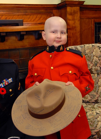 Photo of Keian Blundell wearing red serge and holding autographed RCMP stetson 