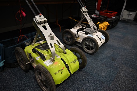 Two large specialized surveying machines on the ground in front of a table with more surveying equipment.