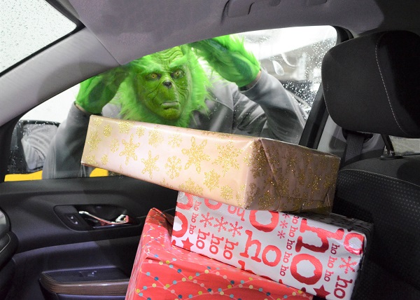 The Grinch peering through the window of a vehicle full of packages and presents