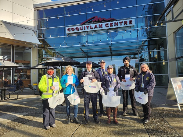 Coquitlam RCMP Community Policing Volunteers, Police officers and ICBC standing outside Coquitlam Centre holding auto crime information packages