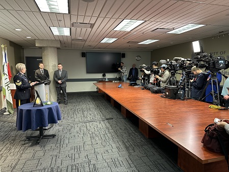 Image of media availability on February 6, 2024, with Surrey RCMP Sgt. Tammy Lobb standing at podium and a row of TV cameras facing her across the room. 