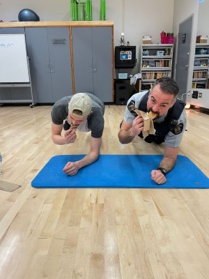 Police officer doing a push up with a teenager while eating a donut