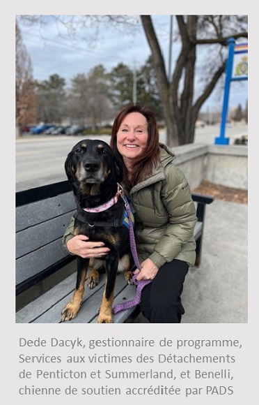 Photo d’une femme blanche assise sur un banc et tenant un chien labrador noir devant une enseigne de la GRC. Sous la photo, on peut lire : Dede Dacyk, gestionnaire de programme, Services aux victimes des Détachements de Penticton et Summerland, et Benelli, chienne de soutien accréditée par PADS